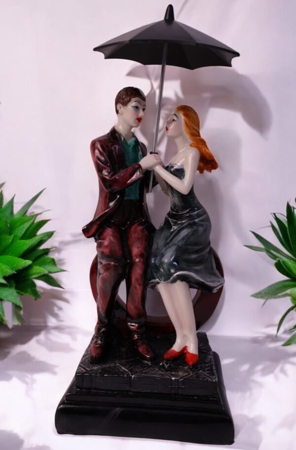 A romantic couple holding sitting on heart shape bench holding umbrella made up of polyresin. A beautiful statue for gifting and showpiece.